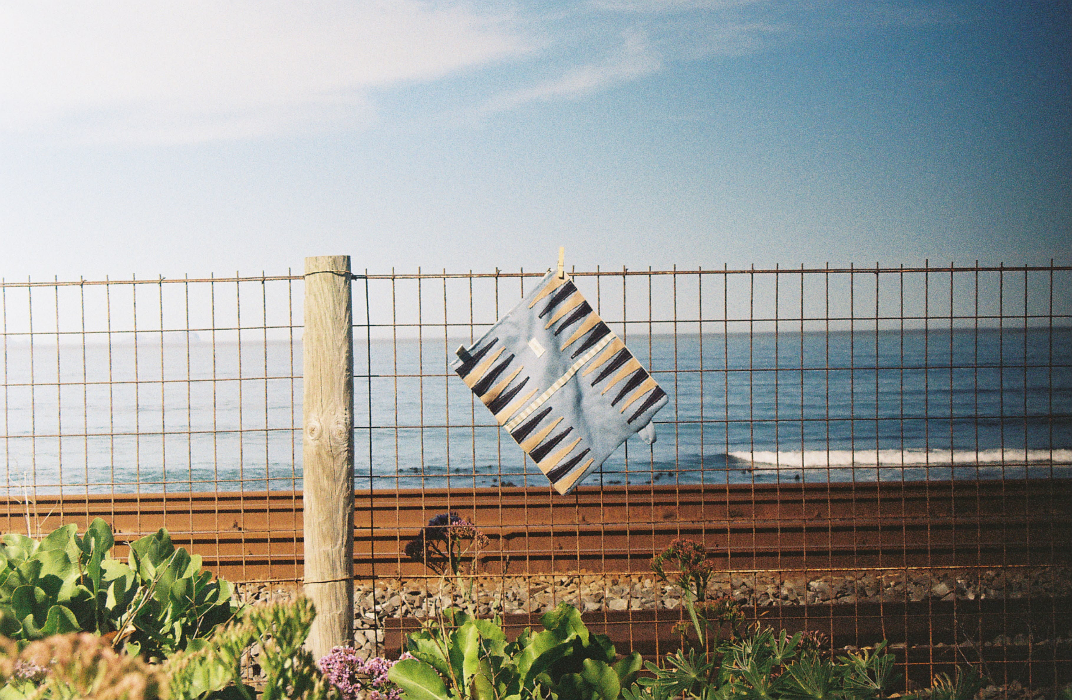 A YourTurn board clipped to a wire fence, railway and ocean behind it.